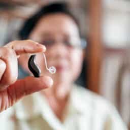 Blurred out senior woman holding up a modern BTE hearing aid