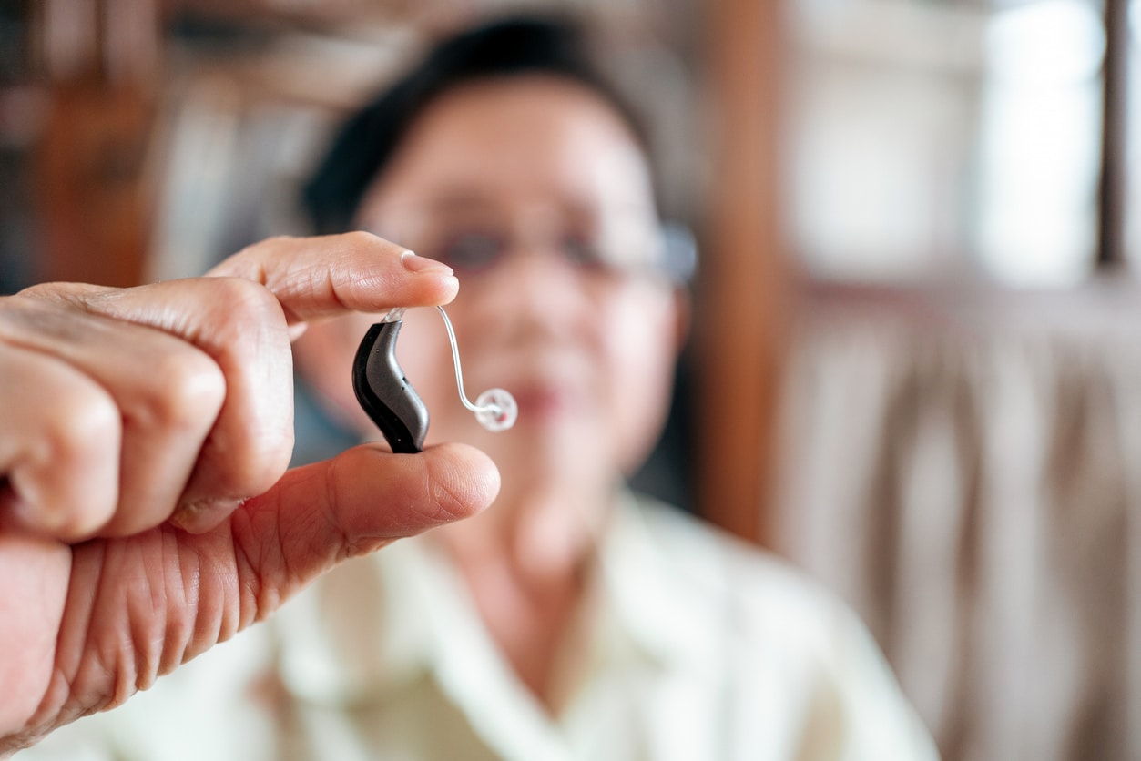 Blurred out senior woman holding up a modern BTE hearing aid