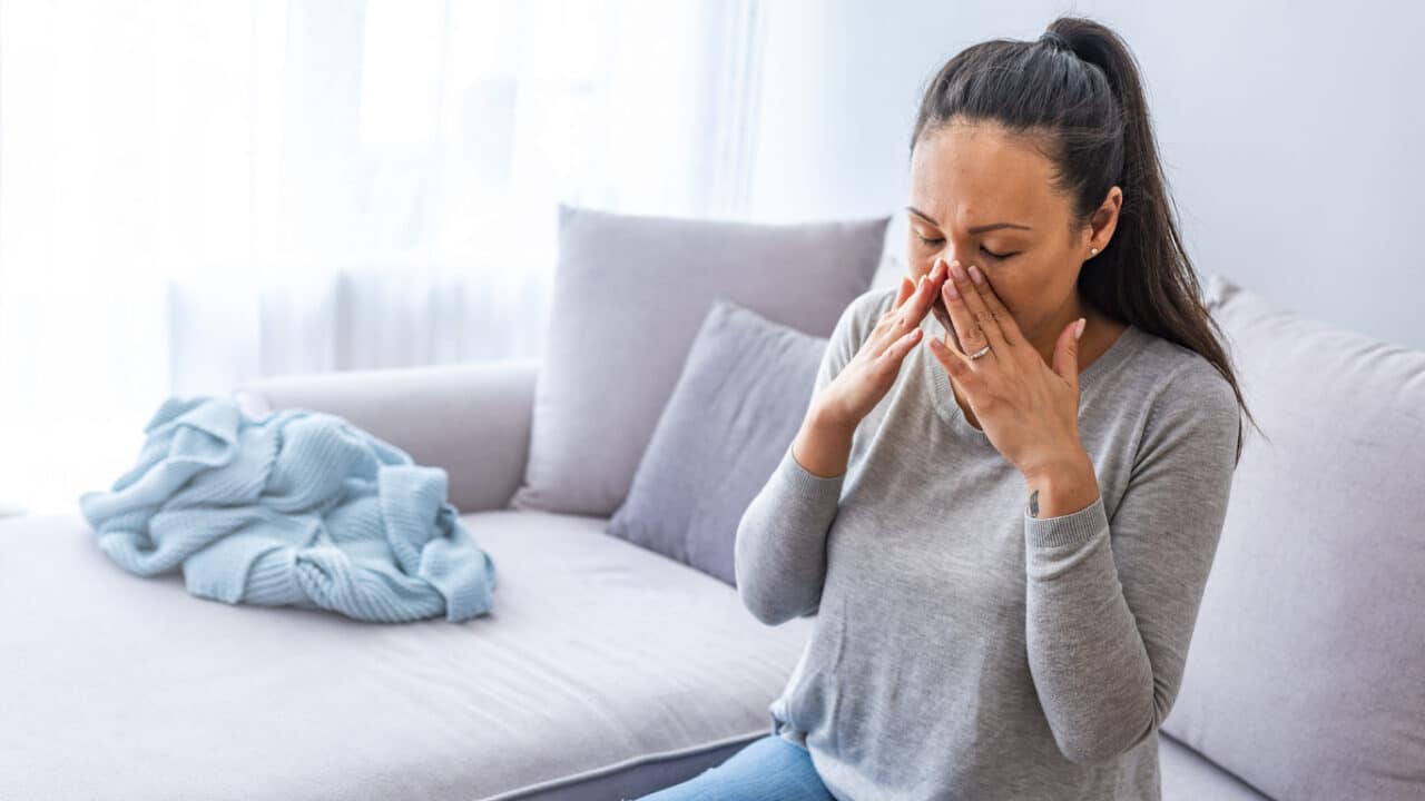 Woman sitting on a couch holding her sore sinuses.