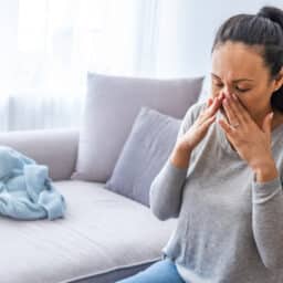 Woman sitting on a couch holding her sore sinuses