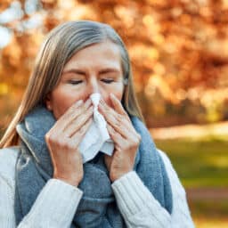Woman with fall allergies blowing her nose in the park