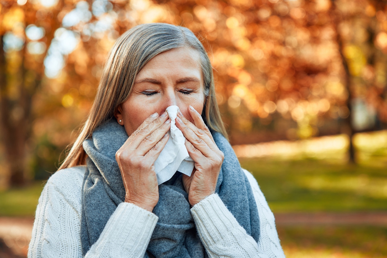 Woman with fall allergies blowing her nose in the park.
